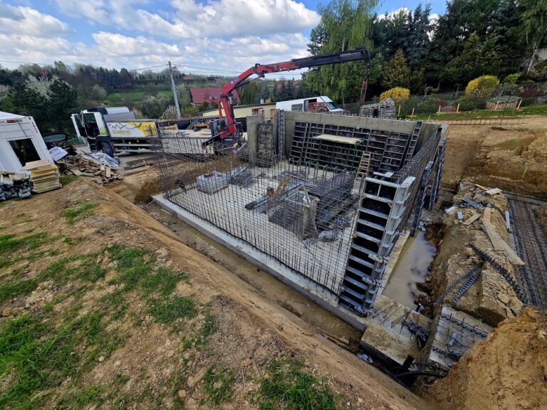 Budowa domu jednorodzinnego Trojanowice - szalunki ścian piwnicy i dźwig HDS dostarczający materiał na plac budowy