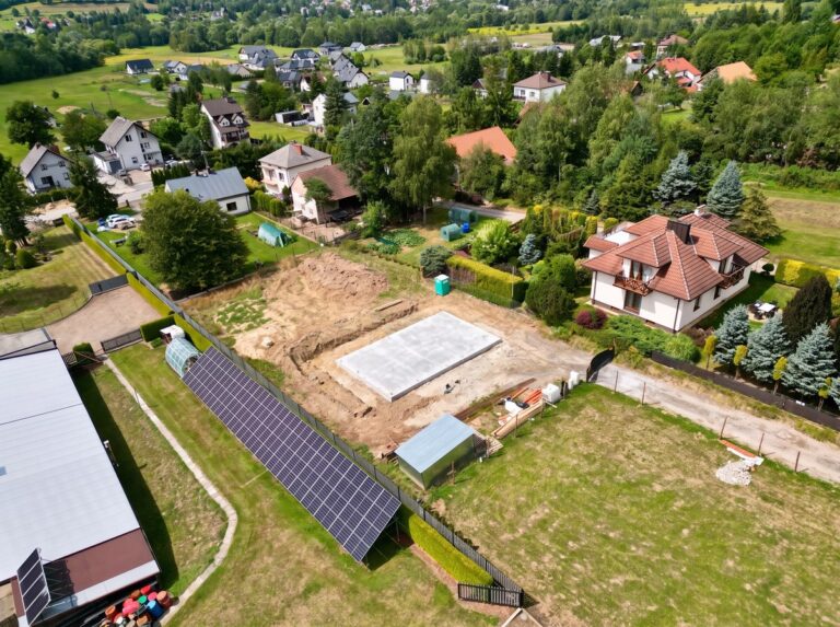 Budowa domu jednorodzinnego Radziszów - płyta z chudego betonu na działce, ujęcie z drona na tle zabudowy